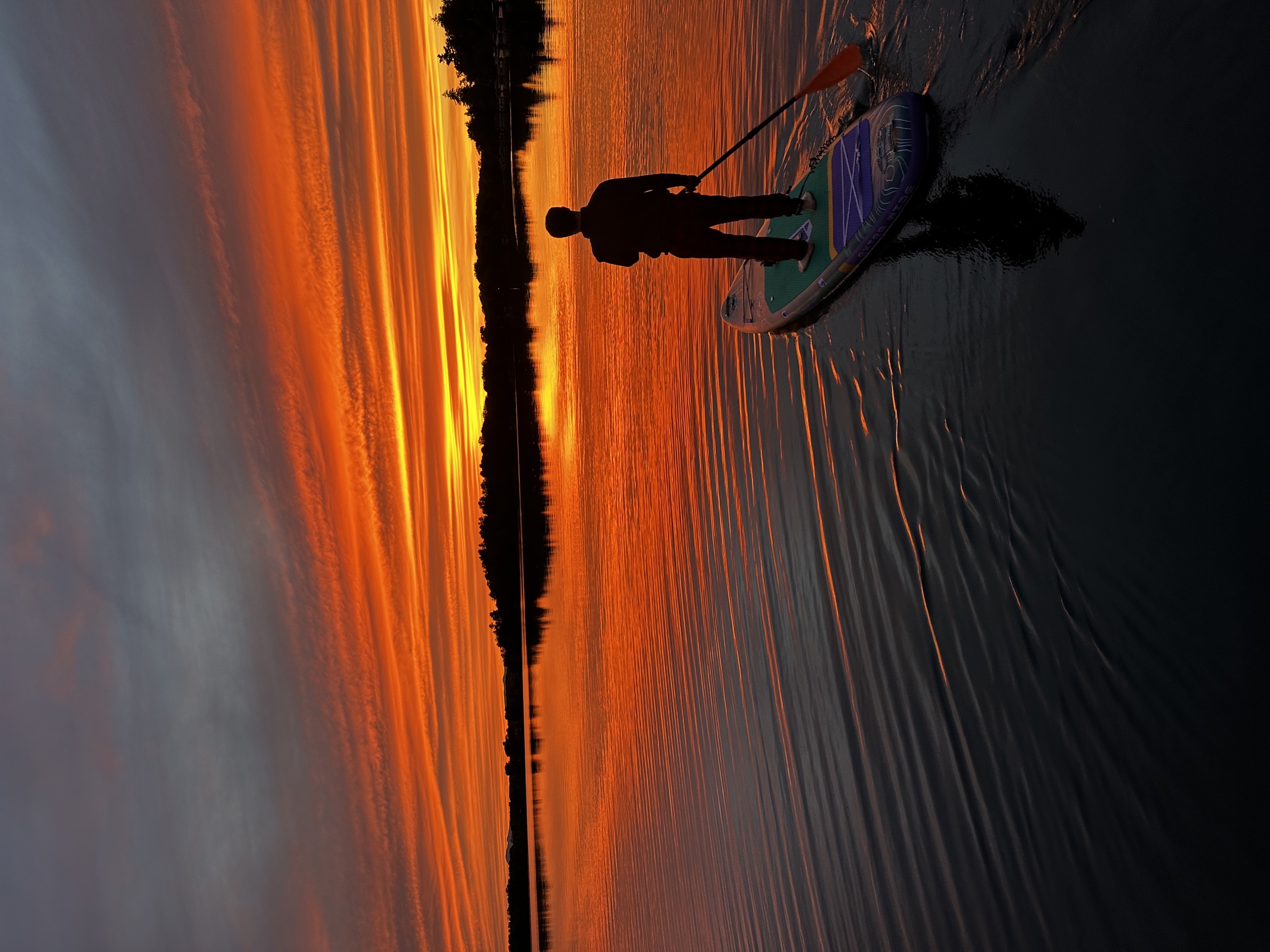 A paddleboarder crossing Copake Lake beneath a vivid evening sky